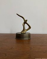 Front view of brass seagull sculpture showing abstract bird shape and circular base on wood surface against white wall.