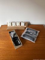 Overview of the six white square cabinet knobs with diagonal metallic line design, black cabinet handles and hardware in original packaging and boxes, displayed on a wooden surface.