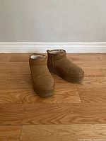 Pair of tan Cushionaire winter boots with fuzzy white lining seen from front angle on wooden floor