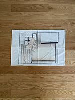 Single pillowcase laid flat on wooden floor showing geometric and floral design with neutral beige, black, and white colors.