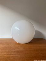 White glass globe lamp shade shown at side angle on wooden surface.