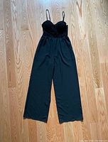 Full view of black jumpsuit laid flat on wood floor showing full length and shape