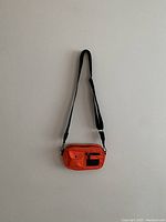 Front view of the small compact orange Markberg Denmark crossbody bag, showing the zippered and snap button pockets along with the black logo patch and adjustable strap.