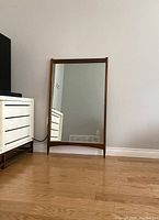 Front view of full-length walnut framed mirror leaning against wall on hardwood floor