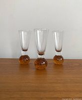Front view of the set of 3 shot glasses showing clear glass upper portion with amber bubble bases, placed on wooden surface.