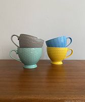 Side view of four mugs stacked in pairs showing various exterior colors and patterns
