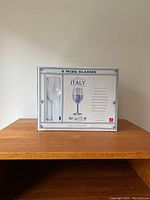 Front view of boxed set of six Italian wine glasses showing one glass through window and decorative text on box