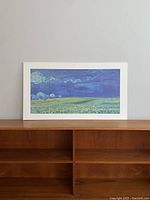 Full view of plaque showing Van Gogh's Wheatfield under Thunderclouds artwork on a wooden shelf.