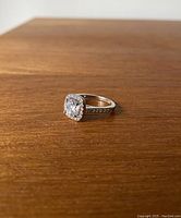 Silver ring with a large clear gemstone surrounded by smaller stones, displayed on a wooden surface.