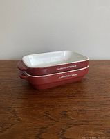Stacked view of two rectangular Lagostina ceramic casserole dishes showing red exterior with white interior and brand name on the side.