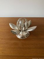 Metallic silver flower-shaped candle holder with petal details on a wooden surface, front view.