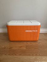 Front view of vintage Coleman PolyLite cooler showing orange ribbed body and white lid with logo.