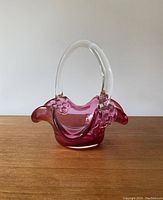 Front angle view of the cranberry glass candy dish basket on wooden surface against plain background