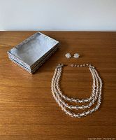 Necklace and earrings displayed flat on wooden surface with decorative box lid placed near them