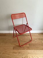 Side view of red metal mesh folding chair showing bent seat and overall structure.