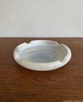 Photo of the vintage large glass ashtray placed on a wooden surface, showing a side angle view that highlights its depth and shape.
