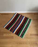 Photo of colorful striped Mexican blanket partially folded on wood floor