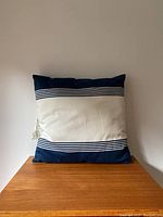 Front view of square pillow showing navy blue and white striped design on a wooden surface against a light wall.