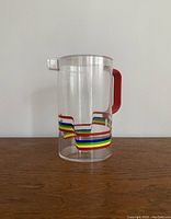 Front view of vintage plastic pitcher showing red handle and rainbow stripes around the base.