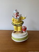 Front view of the clown figurine standing on a round base showing colorful attire, clown and piglet detail.