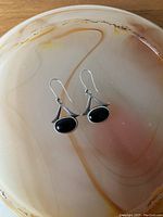 Close-up photo showing the pair of vintage sterling silver earrings with oval black onyx stones and triangular silver accents, laying on a reddish beige stone background.