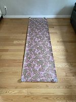 Full view of the wallpaper roll laid out on a wooden floor, showing floral pattern primarily in pink and beige.