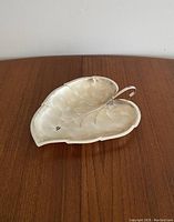 Leaf-shaped metal dish or tray placed on wooden surface, showing overall form, shape, and design.