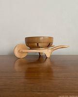 Side profile view of the vintage wooden wheelbarrow bowl resting on wooden surface against gray wall.