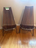 Two acacia wood folding chairs placed side by side on hardwood floor, showing slatted backrest and seat design