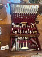 Image showing cutlery and servingware in wooden box with knives on top part of box and various forks, spoons, and serving utensils in lower compartments lined with red velvet.