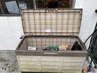 View of closed plastic deck box, beige with brown lid, outdoors showing dirt and wear
