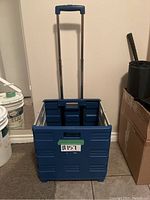 Blue folding crate unfolded showing telescoping handle extended and wheels on bottom.