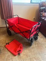 Side angle photo of red folding utility cart with carrying case on floor
