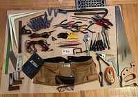 Full view of tools spread on floor including pliers, clamps, screwdrivers, calipers, adjustable wrench, tool belt, saw, measuring tape, and other hand tools.