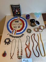 Full lot of jewelry items displayed on table with book, highlighting the range of necklaces, earrings, bracelets, and pendants.