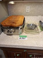 KitchenAid roasting pans stacked, wooden cutting board on top, Pyrex baking dish and strainer placed next to pans on countertop