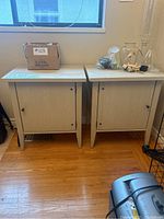 Two light stained wood nightstands side by side under window, some items on top including a box and glassware (not included).
