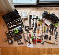 Complete overhead view of all tools, including hammers, axes, chisels, tapes, and screwdriver set on tan paper.