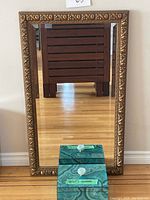 Full view of large rectangular mirror with thick decorative gold-tone frame along with teal velvet lined decorative box placed in front