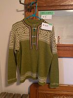 Full view of the green Norwegian style sweater with white pattern, hanging on a hanger.