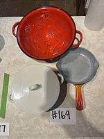 Top view of red enamel colander, speckled skillet, and casserole lid on countertop