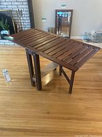 Wood folding table set up showing slatted tabletop and folding leg design.