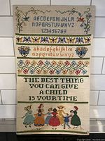 Full view of the vintage cross stitch sampler showing alphabets, numbers, floral bands, quote, and children figures.