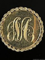 Front view showing engraved monogram with braided edge on the circular gold filled pin.