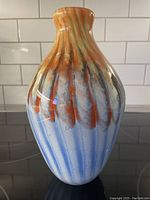 Front view of the glass vase showing blue, orange, and gold channeled glass design over a white base with a rounded shape and narrow opening.