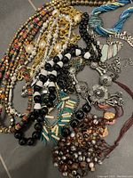 Collection of various beaded necklaces and chains with multiple colors and textures visible, including metallic beads and multi-colored strings.