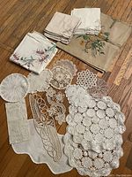 Various linens arranged on wooden floor showing crocheted doilies, embroidered cloths and lace pieces