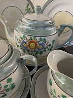 Close-up photo of teapot, creamer and sugar with floral hand painted design and lustrous silver trim.