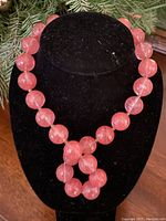 Full view of necklace displayed on black bust showing the strand of round pink faceted beads and signed toggle closure.