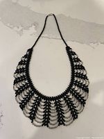 Full photo of lavalier style necklace made of black and clear micro beads with a lace collar design, laid flat against a light background